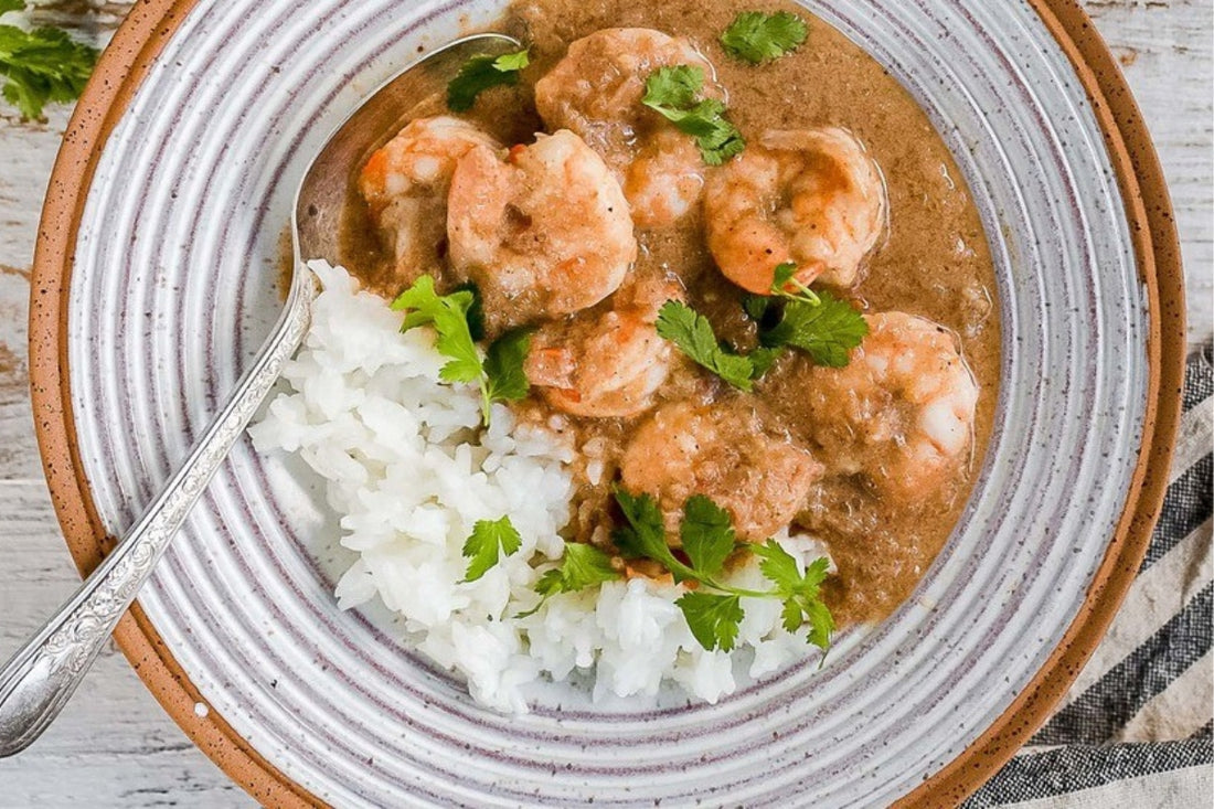 Malai king prawn curry with jasmine rice served with fresh coriander on the top in a ceramic bowl with white glaze and brown edging