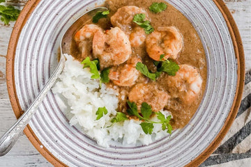 Malai king prawn curry with jasmine rice served with fresh coriander on the top in a ceramic bowl with white glaze and brown edging