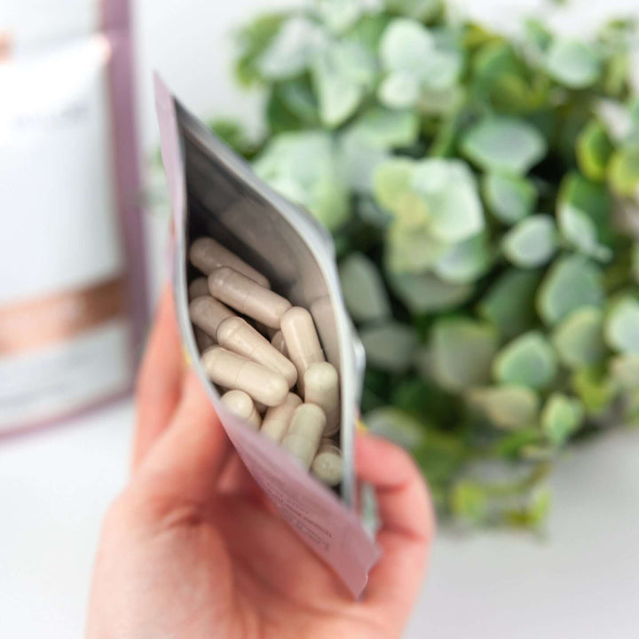 close up image of Birch & Wilde selenium capsule health supplement refill pouches. One pouch is standing up and the other is open and the capsules inside are visible from above. 