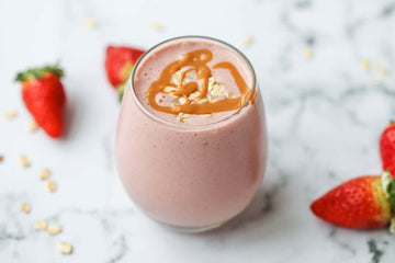 Image of a pink strawberry protein smoothie served in a glass with fresh strawberries scattered around it