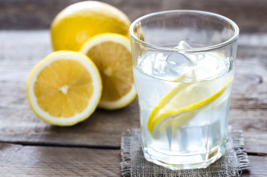image to show good hydration with a large glass of clear water with bright yellow lemon slices in it and a freshly cut lemon next to it