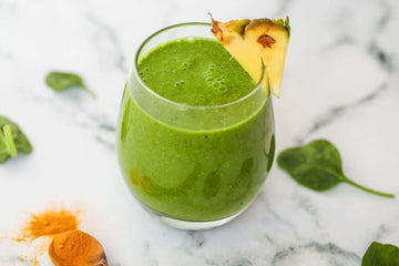 Image of an Anti-Inflammatory Green Chia Seed Smoothie served in a glass with a slice of pineapple garnish and turmeric scatted close to the glass