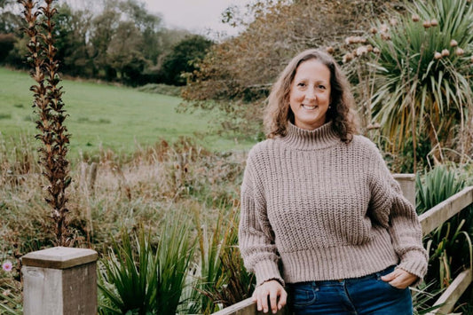 Tara Barton the founder of birch and wilde supplements standing against a wooden fence with a green field behind wearing a brown wool jumper