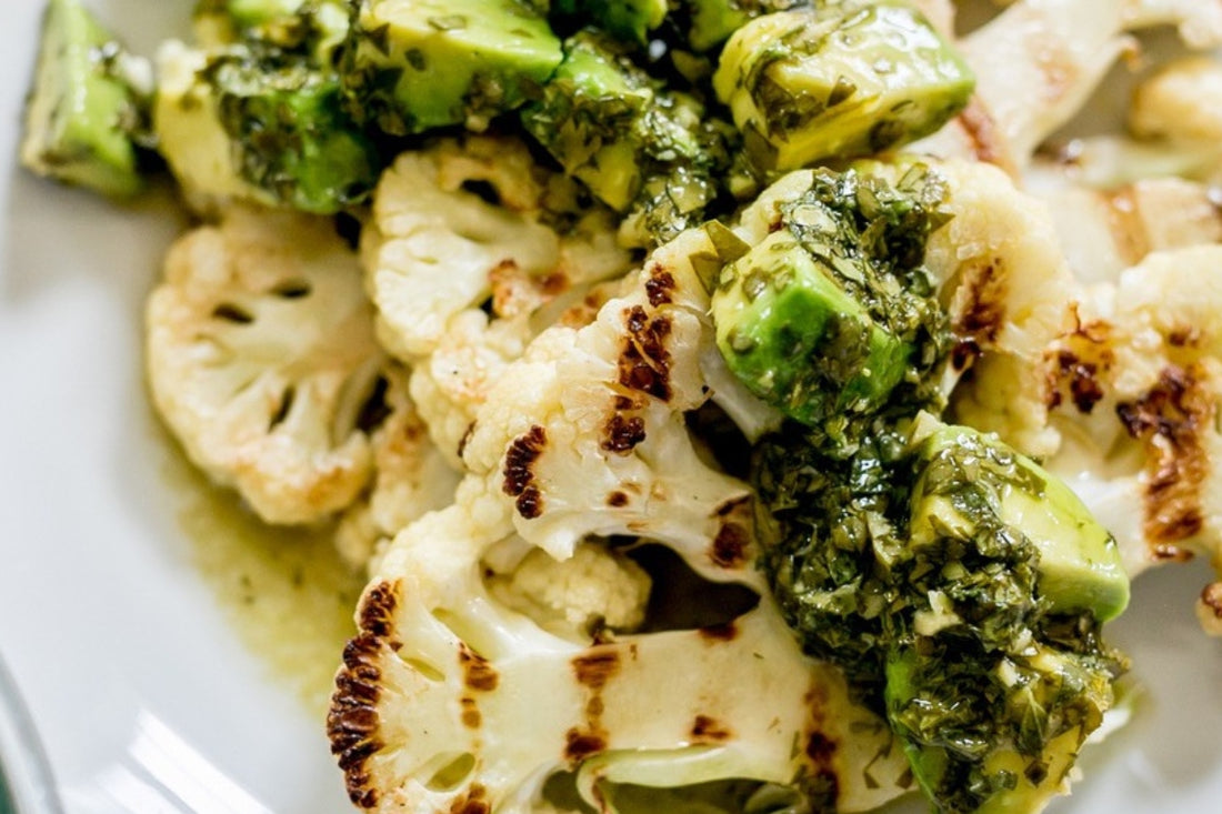 Chargrilled cauliflower steaks dressed with homemade avocado chimichurri over the top, on a white plate, view close up from above