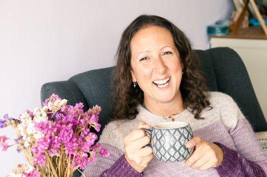 image of Birch & Wilde supplements and nutrition brand founder sitting in her favourite chairs and smiling while holding a big grey mug of tea with pink purple and white flowers next to her