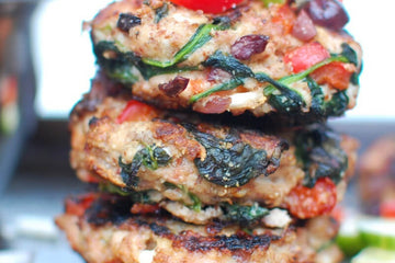 close up image of barbequed greek style chicken burgers with olives red peppers and feta cheese