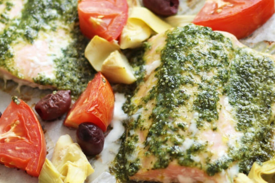 Image of one pan Mediterranean trout topped with home made pesto and surrounded with roast tomatoes and vegetables on a white plate