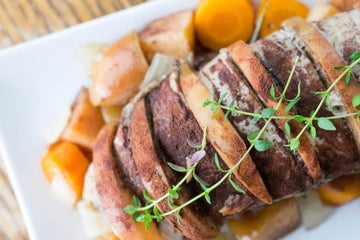 Image from above of a pork tenderloin fillied with apple slices sitting on a bed of mixed root vegetables on a white ceramic plate