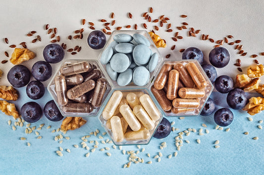 flatlay view from above of a selections of supplements capsules and pills with fresh blueberries against a white and light blue background