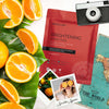flat lay product shot of front of a beautypro brightening collagen face sheet mask with oranges and a travel camera