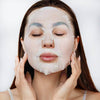 head shot of woman with long dark hair applying a sheet mask away to her face