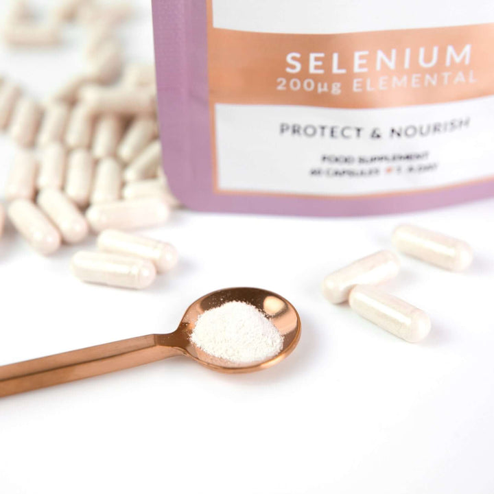 close up image of Birch & Wilde selenium capsule health supplement refill pouch. Some selenium capsules are around the bottom of the pouch as well as selenium powder in a rose gold spoon. 