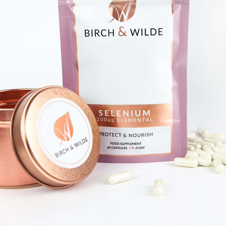 product lifestyle shot taken from the front of Birch & Wilde selenium health supplement capsule refill pouch with capsules lying around it and a rose gold refill tin to one side